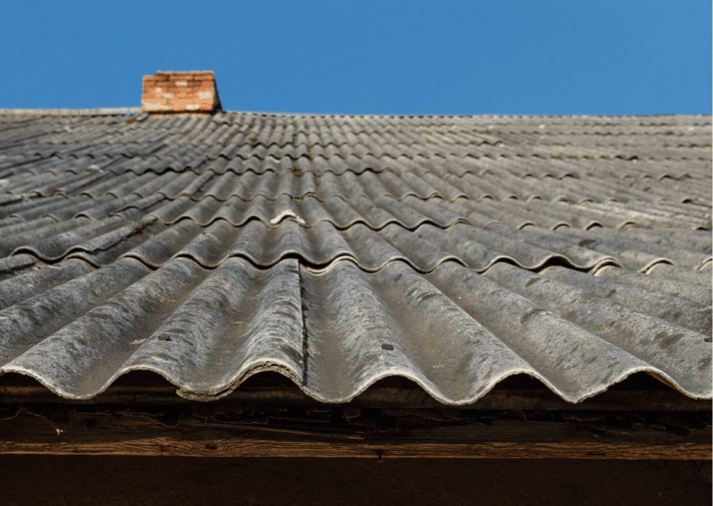 Detailed close-up of an aging corrugated asbestos cement roof sheet showing fine cracks, flaking, and a fibrous, weathered texture.